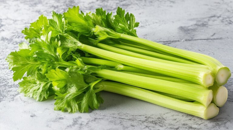 A fresh bunch of bright green celery stalks with leaves, laid on a light-colored countertop, ready for use in cooking or snacking.